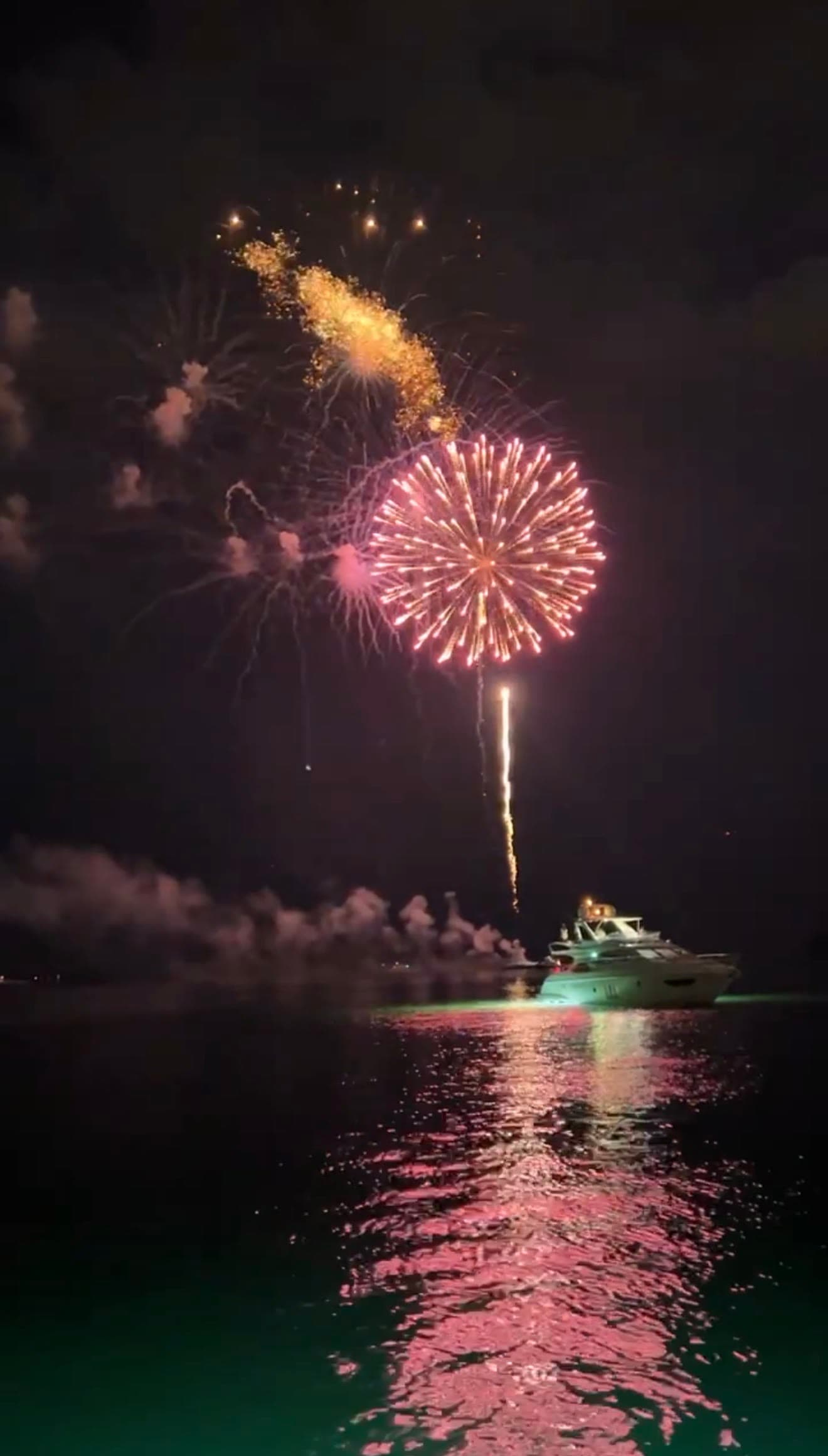 Fireworks illuminating the water beside a yacht at night